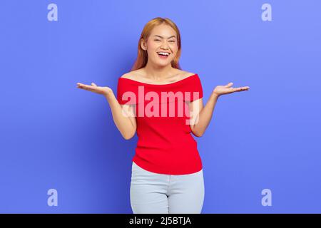 Porträt einer aufgeregten asiatischen Frau, die mit einer Handfläche zur Seite zeigt und den Kopierraum auf einem violetten Hintergrund zeigt Stockfoto