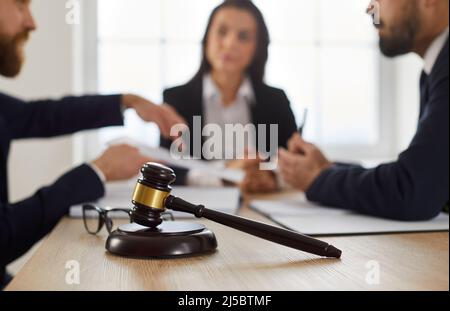 Richterhammer auf dem Tisch, mit Rechtsanwalt, der im Hintergrund Rechtsberatung für Kunden gibt Stockfoto