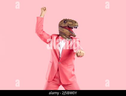 Lustige verrückte Mann in rosa Anzug und Dinosaurier-Maske tanzen isoliert auf rosa Hintergrund Stockfoto