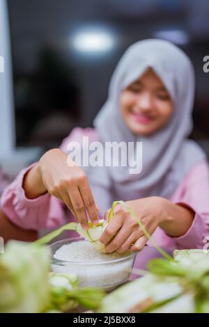 Schöne muslimische Frau, die Ketupat für idul fitri macht Stockfoto
