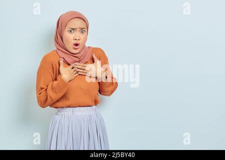 Porträt der überrascht schönen asiatischen Frau in braunen Pullover und Hijab mit Hand auf Brust isoliert auf weißem Hintergrund Stockfoto