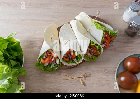 Köstliche Tortillas mit Hühnerfilets und Gemüse auf dem Küchentisch und Holztisch. Diätetische Ernährung Stockfoto