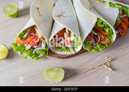 Eingewickelte Tortillas mit frischem Salat, Paprika, Tomaten und Hühnerfilets auf dem heimischen Küchentisch. Vegetarisches Essen Stockfoto