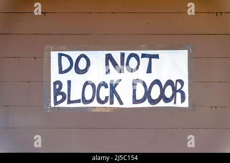 Blockieren Sie nicht die Türschilder an einer braunen Holzwand in San Francisco, Kalifornien. Handschriftliche Vorsicht auf einem weißen Papier, das an einer Gebäudewand geklebt ist. Stockfoto