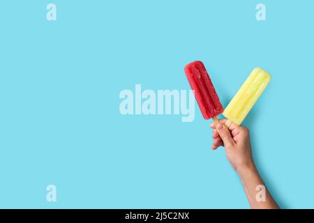 Hand mit Erdbeer- und Zitronenlippesikeln auf blauem Hintergrund Stockfoto