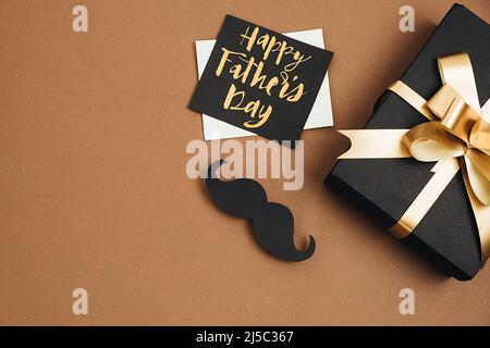 Horizontale Bilder von handgefertigten schwarzen Geschenkkarton, Karte mit Phrase Happy Father's day und Retro stilvolles schwarzes Papier Fotokabine Requisiten Schnurrbärte auf braun Stockfoto