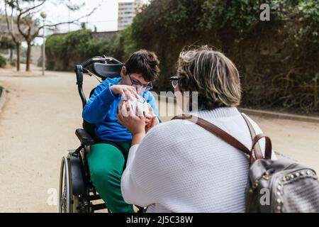 Junge mit mehreren Behinderungen spielt mit seiner Mutter im Park mit einem Fußball. Stockfoto