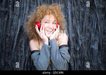 Junge lateinerin mit lockigen afro Haaren, die mit roten Kopfhörern Musik hört Stockfoto