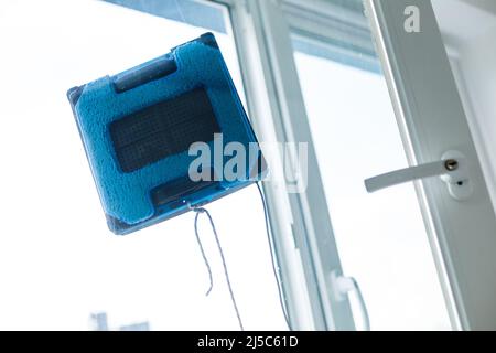 Glasreinigungsroboter, der unter dem Blick eines Teddybären im Schlafzimmerfenster arbeitet Stockfoto