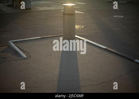 Urne auf dem Parkplatz. Ort, um Müll auf der Straße zu sammeln. Schatten von Müll auf Asphalt. Parkdetails. Stockfoto