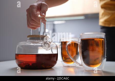 Schwarzer Tee in einer transparenten Teekannen und Tassen in der Nähe Stockfoto
