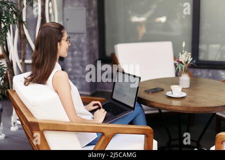 Lächelnde junge Frau, die auf ihrem Laptop E-Mails durchstöbert. Stockfoto