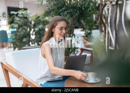Lächelnde junge Frau trinkt Kaffee in einem gemütlichen Café. Stockfoto