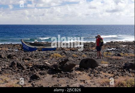 Fotograf, der Fotos von verlassenen Fischerbooten an der Küste in der Nähe von Costa Teguise, Lanzarote, den Kanarischen Inseln, Spanien macht. Februar 2022. Im Winter Stockfoto