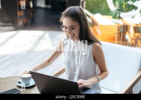 Lächelnde junge Frau trinkt Kaffee in einem gemütlichen Café. Stockfoto