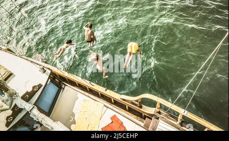 Luftaufnahme der jungen Leute, die auf einem Seetrip vom Segelboot springen - reiche glückliche Freunde, die im Sommer Spaß am Segelbootparty haben - Exklusive Luxusvaca Stockfoto