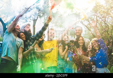 Fröhliche Freunde, die sich auf einer Gartenparty mit bunten Rauchbomben im Freien amüsieren - Junge Millennials-Studenten feiern gemeinsam die Frühlingsferien - echt Stockfoto