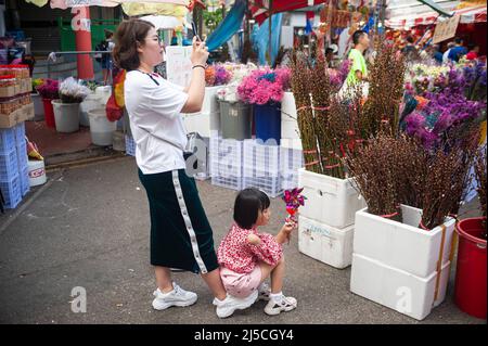 24. Januar 2020, Singapur, Republik Singapur, Asien - Eine Frau fotografiert mit ihrem Handy auf einem Straßenmarkt in Chinatown, während ihre junge Tochter mit einem Windrad auf dem Fuß sitzt. [Automatisierte Übersetzung] Stockfoto