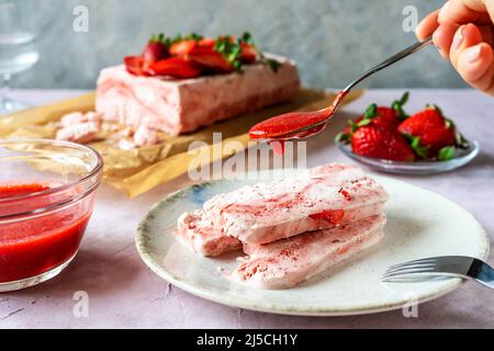 Italienisches Erdbeerdessert Semifreddo auf dem Teller mit menschlicher Hand und Teelöffel mit Erdbeersoße Stockfoto