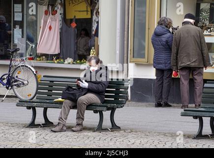 Eine ältere Frau mit Gesichtsmaske sitzt auf einer Bank in einer Berliner Fußgängerzone. Aufgrund des Coronavirus müssen die Menschen einen sicheren Abstand zueinander halten. [Automatisierte Übersetzung] Stockfoto