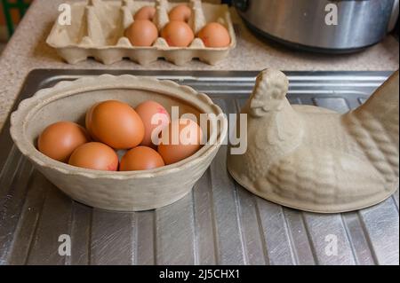 Eier in einem Keramikkorb in Hühnerform und Kartonverpackung auf Küchentisch Abtropfbrett im Haus. Stockfoto