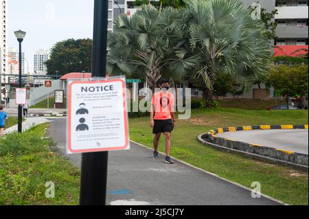 29. April 2020, Singapur, Republik Singapur, Asien - Ein Mann mit Mundschutz kommt an einem Covid-19-Schild vorbei, das verbindliche Maßnahmen zur weiteren Begrenzung der Ausbreitung des Coronavirus anzeigt. Mit Ausnahme von körperlich anspruchsvollen Aktivitäten wie Radfahren oder Joggen muss jeder bei Verlassen seines Zuhauses und im Freien oder in der Öffentlichkeit jederzeit einen Mundschutz tragen. [Automatisierte Übersetzung] Stockfoto