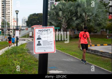 29. April 2020, Singapur, Republik Singapur, Asien - Ein Mann mit Mundschutz kommt an einem Covid-19-Schild vorbei, das verbindliche Maßnahmen zur weiteren Begrenzung der Ausbreitung des Coronavirus anzeigt. Mit Ausnahme von körperlich anspruchsvollen Aktivitäten wie Radfahren oder Joggen muss jeder bei Verlassen seines Zuhauses und im Freien oder in der Öffentlichkeit jederzeit einen Mundschutz tragen. [Automatisierte Übersetzung] Stockfoto