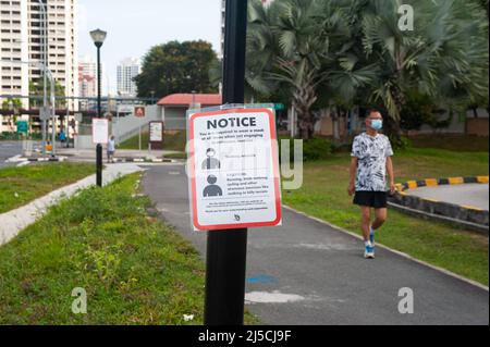 29. April 2020, Singapur, Republik Singapur, Asien - Ein Mann mit Mundschutz kommt an einem Covid-19-Schild vorbei, das verbindliche Maßnahmen zur weiteren Begrenzung der Ausbreitung des Coronavirus anzeigt. Mit Ausnahme von körperlich anspruchsvollen Aktivitäten wie Radfahren oder Joggen muss jeder bei Verlassen seines Zuhauses und im Freien oder in der Öffentlichkeit jederzeit einen Mundschutz tragen. [Automatisierte Übersetzung] Stockfoto