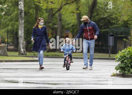 Endlich raus - Familie trägt Gesichtsmasken in einem öffentlichen Park, während sie mit ihrer kleinen Tochter Fahrrad fahren. [Automatisierte Übersetzung] Stockfoto