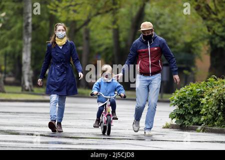 Endlich raus - Familie trägt Gesichtsmasken in einem öffentlichen Park, während sie mit ihrer kleinen Tochter Fahrrad fahren. [Automatisierte Übersetzung] Stockfoto