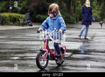 Endlich raus - Familie trägt Gesichtsmasken in einem öffentlichen Park, während sie mit ihrer kleinen Tochter Fahrrad fahren. [Automatisierte Übersetzung] Stockfoto