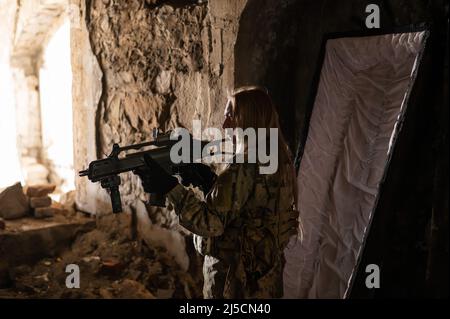 Kaukasische Frau in Armeeuniform, die ein Maschinengewehr hält und in der Nähe eines offenen Sarges steht. Stockfoto