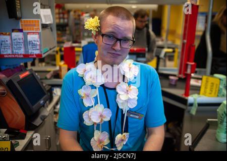 06/23/2018, Helsinki, Finnland, Europa - Anlässlich des Hochsommers schmücken sich viele Einheimische mit Blumenkränzen und Blumenhalsketten, wie dieser junge Mann, der an der Kasse eines Supermarkts arbeitet. [Automatisierte Übersetzung] Stockfoto