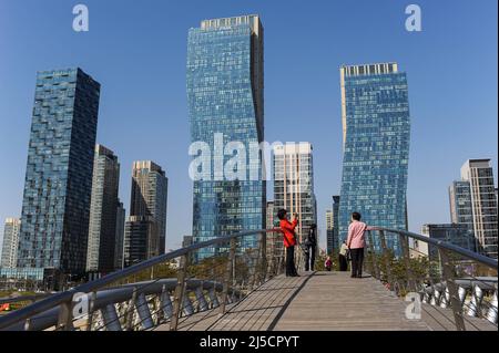 01.05.2013, Seoul, Südkorea, Asien - Menschen auf einer Brücke vor dem Blick auf die Stadt New Songdo City im Central Park und dem internationalen Geschäftsviertel mit modernen Wohntürmen. Der neue Stadtteil wurde als geplante Stadt konzipiert und ist Teil der Megacity Incheon. Sie umfasst etwa 610 Hektar Land, das vom Meer zurückgewonnen wird und liegt etwa 40 Kilometer südwestlich des Zentrums der Hauptstadt Seoul. Zusammen mit Yeongjong und Cheongna bildet der Bezirk die Incheon Free Economic Zone. [Automatisierte Übersetzung] Stockfoto