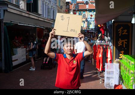 24. Januar 2020, Singapur, Republik Singapur, Asien - Ein Verkäufer hält zu Beginn der Corona-Krise ein Pappschild mit einem Sparangebot hoch, während die Menschen durch einen belebten Straßenbasar im Chinatown-Viertel der Stadt schlendern, der jährlich zum chinesischen Neujahr stattfindet. Kurz nachdem der Stadtstaat seine erste Infektion mit dem Coronavirus bestätigt hatte (Covid-19). [Automatisierte Übersetzung] Stockfoto