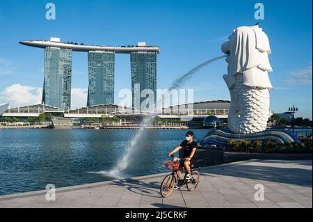 23. September 2020, Singapur, Republik Singapur, Asien - Ein Radfahrer mit Mundschutz fährt durch den Merlion Park mit der Brunnenstatue am Ufer des Singapore River, während das Marina Bay Sands Hotel im Hintergrund zu sehen ist. [Automatisierte Übersetzung] Stockfoto