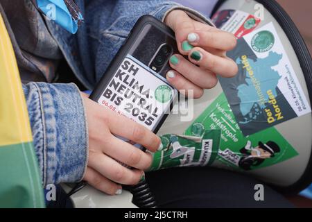 Brunsbuttel, Deutschland. 22. April 2022. 22. April 2022, Schleswig-Holstein, Brunsbüttel: Ein Klimaaktivist von Fridays for Future hält während einer Demonstration gegen das geplante LNG-Terminal in Brunsbüttel ein Handy. Das Terminal soll spätestens 2026 in Betrieb gehen und eine Kapazität von 8 Milliarden Kubikmetern Gas haben. Angesichts des Krieges in der Ukraine will die Bundesregierung die Abhängigkeit Deutschlands von russischem Erdgas so schnell wie möglich beenden. Foto: Marcus Brandt/dpa Quelle: dpa picture Alliance/Alamy Live News Stockfoto