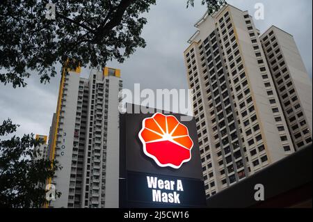 14. Dezember 2020, Singapur, Republik Singapur, Asien - an einer Tankstelle in einem Wohngebiet weist ein beleuchtetes Schild mit der Aufschrift „Wear A Mask“ auf die allgemeine Anforderung hin, an öffentlichen Orten eine Maske zu tragen, um eine weitere Ausbreitung des Coronavirus (Covid-19) während der globalen Coronapandemie zu verhindern. Im Hintergrund erheben sich Hochhausgebäude. [Automatisierte Übersetzung] Stockfoto