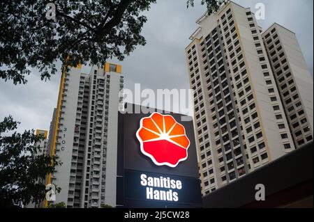 14. Dezember 2020, Singapur, Republik Singapur, Asien - an einer Tankstelle in einem Wohngebiet weist ein beleuchtetes Schild mit der Aufschrift „Hände desinfizieren“ auf Hygienevorschriften hin, um eine weitere Ausbreitung des Coronavirus (Covid-19) während der globalen Coronapandemie zu verhindern. Im Hintergrund erheben sich Hochhausgebäude. [Automatisierte Übersetzung] Stockfoto