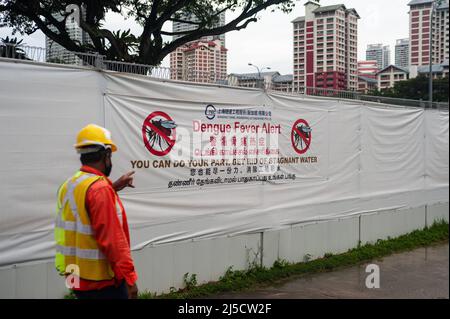 14. Dezember 2020, Singapur, Republik Singapur, Asien - Ein Arbeiter geht an einer Baustelle in einer Wohngegend vorbei, wo ein großes Banner auf dem Bauzaun vor der Gefahr warnt, dass sich Dengue-Fieber von Mücken ausbreitet und anzieht, Da sie stehendes Wasser wie das auf Baustellen gefundene als mögliche Brutplätze nutzen. [Automatisierte Übersetzung] Stockfoto