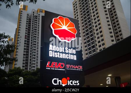 14. Dezember 2020, Singapur, Republik Singapur, Asien - an einer Tankstelle in einem Wohngebiet weist ein beleuchtetes Schild mit der Aufschrift „Adopt Safe Distancing“ auf die allgemein gültigen Entfernungsregeln in öffentlichen Räumen hin, um eine weitere Ausbreitung des Coronavirus (Covid-19) während der globalen Coronapandemie zu verhindern. Im Hintergrund erheben sich Hochhausgebäude. [Automatisierte Übersetzung] Stockfoto