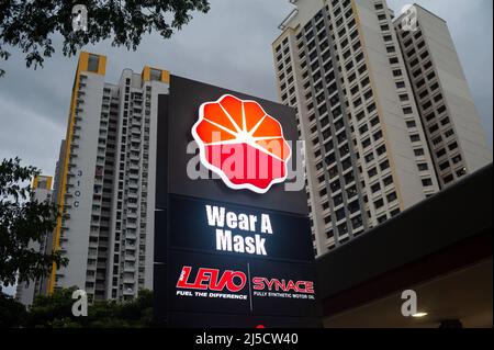 14. Dezember 2020, Singapur, Republik Singapur, Asien - an einer Tankstelle in einem Wohngebiet weist ein beleuchtetes Schild mit der Aufschrift „Wear A Mask“ auf die allgemeine Anforderung hin, an öffentlichen Orten eine Maske zu tragen, um eine weitere Ausbreitung des Coronavirus (Covid-19) während der globalen Coronapandemie zu verhindern. Im Hintergrund erheben sich Hochhausgebäude. [Automatisierte Übersetzung] Stockfoto