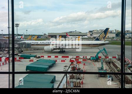 08. Dezember 2020, Singapur, Republik Singapur, Asien - Bauarbeiten am Vorfeld am Terminal 1 des Changi International Airport während der anhaltenden Coronavirus-Krise, mit einem Passagierflugzeug der staatlichen Singapore Airlines im Hintergrund. Die weltweite Ausbreitung des Coronavirus (Covid-19) hat die Anzahl der Flüge weltweit drastisch reduziert, was zu erheblichen Flugausfällen führte. SIA betreibt derzeit nur einen Bruchteil seines Streckennetzes, während die meisten Flugzeuge weiterhin am Boden arbeiten. Die Behörden in Singapur und Hongkong haben bereits Vorkehrungen für die Quarantänefreiheit getroffen Stockfoto