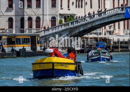 Arbeitsboote transportieren Müll (in ukrainischer Farbe) und Güter auf dem Canale Grande - die Kanäle sind die Hauptarterien für alle Formen des Wassertransports - Venedig zu Beginn der Biennale di Venezia im Jahr 2022. Stockfoto