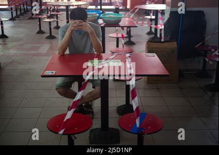25. Mai 2021, Singapur, Republik Singapur, Asien - Ein Mann mit einem Mundschutz sitzt an einem mit flatterndem Klebeband abgesperrten Tisch im Essbereich eines Food Court- und Hawker-Centers in Chinatown während der andauernden Corona-Krise (Covid-19), Kurz nachdem eine neue Infektionswelle das südostasiatische Land in einen Lockdown-ähnlichen Zustand zurückversetzt hat. Dies führte zu weiteren Einschränkungen wie strengeren Grenzmaßnahmen und Einreisebestimmungen in Verbindung mit obligatorischen Vortests und einem negativen Testergebnis bei der Abreise für alle Anwohner und Festanwohner sowie der Schließung aller elementaren Stockfoto