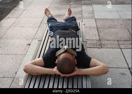 07/11/2019, Singapur, Republik Singapur, Asien - Ein Mann liegt auf einer Bank am Ufer des Singapore River und bedeckt seine Augen mit einem Geldbeutel. [Automatisierte Übersetzung] Stockfoto
