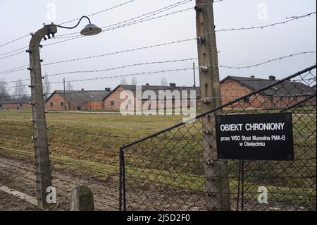 03/16/2015, Auschwitz, Kleinpolen, Polen, Europa - Ein hoher Elektrozaun mit Stacheldraht umgibt das ehemalige Konzentrationslager Auschwitz-II-Birkenau mit leeren Kasernen im Hintergrund. Das Lager in Birkenau diente der SS als Vernichtungslager. [Automatisierte Übersetzung] Stockfoto