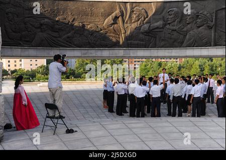 08.08.2012, Pjoengjang, Nordkorea, Asien - Eine Gruppe nordkoreanischer Studenten steht während eines Propaganda-Fotoshootings unter einem riesigen Bronzerelief am Denkmal zur Gründung der Arbeiterpartei Koreas. [Automatisierte Übersetzung] Stockfoto