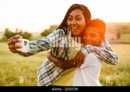 Schwarze Mutter, die während des Picknicks mit ihrem Sohn ein Selfie-Foto auf dem Handy gemacht hat Stockfoto