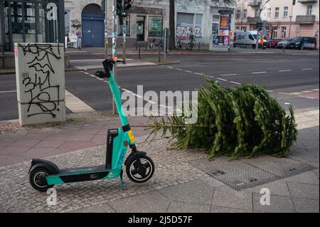 11. Januar 2022, Berlin, Deutschland, Europa - Ein abgenutzter Weihnachtsbaum ohne Christbaumschmuck liegt am Straßenrand in einem Wohngebiet im Bezirk Mitte, das von der Berliner Stadteinigung (BSR) zur Abholung bereitsteht. Daneben steht ein vermietbarer Elektroroller. [Automatisierte Übersetzung] Stockfoto